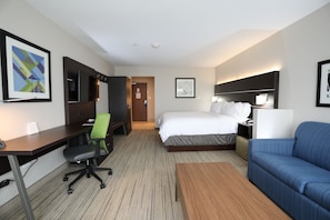 Una habitación de hotel con una cama, un escritorio, una silla, un sofá y dos cuadros en las paredes.