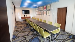 Une salle de conférence avec une longue table, des chaises jaunes, une moquette à motifs et des œuvres d’art encadrées accrochées au mur.