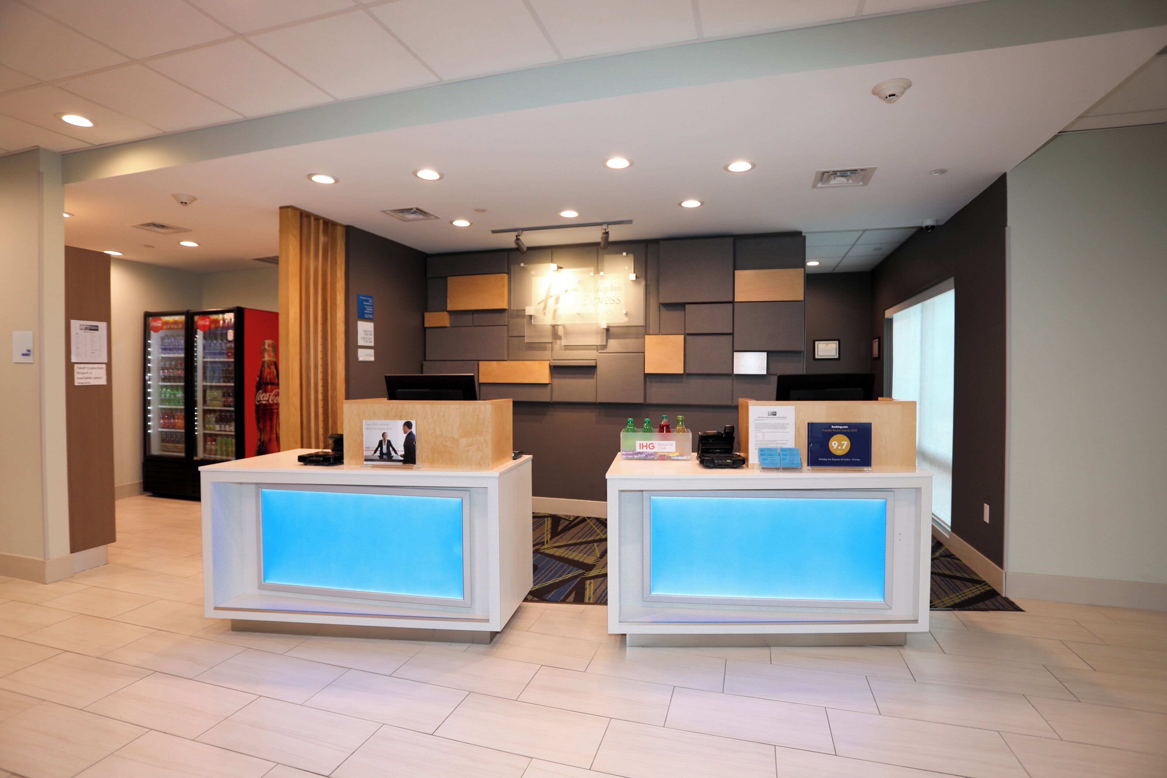 A reception area with two reception desks, a Coca-Cola refrigerator, and a wall-mounted light fixture.