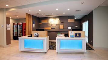 A reception area with two reception desks, a Coca-Cola refrigerator, and a wall-mounted light fixture.