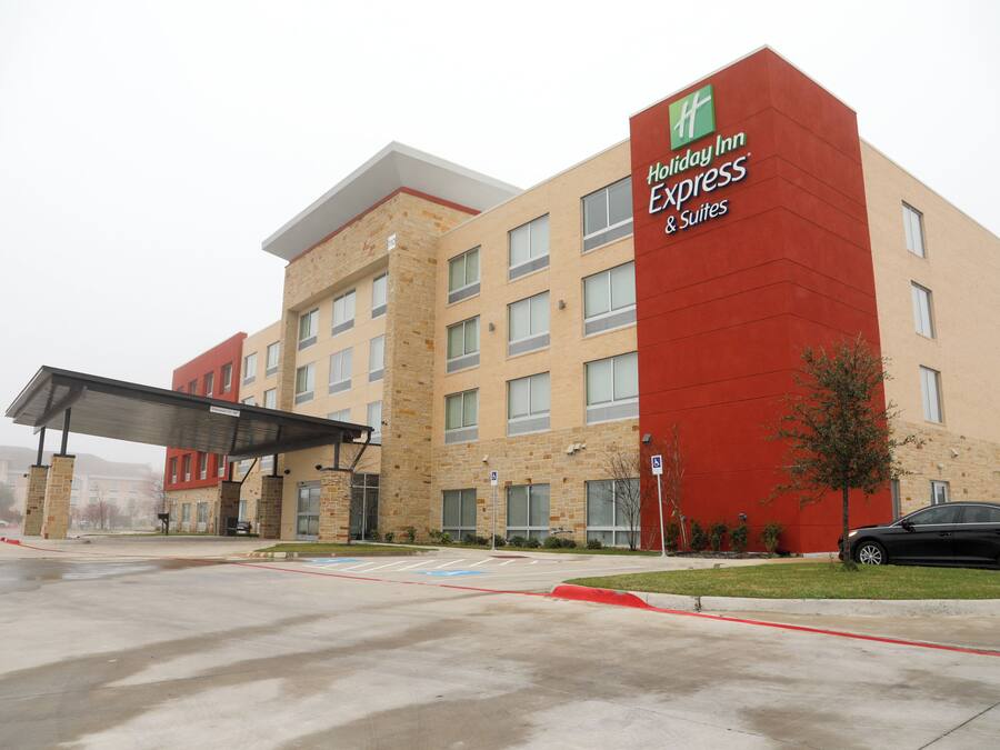 A Holiday Inn Express & Suites hotel with a red and beige facade, a covered entrance, and a parking lot.