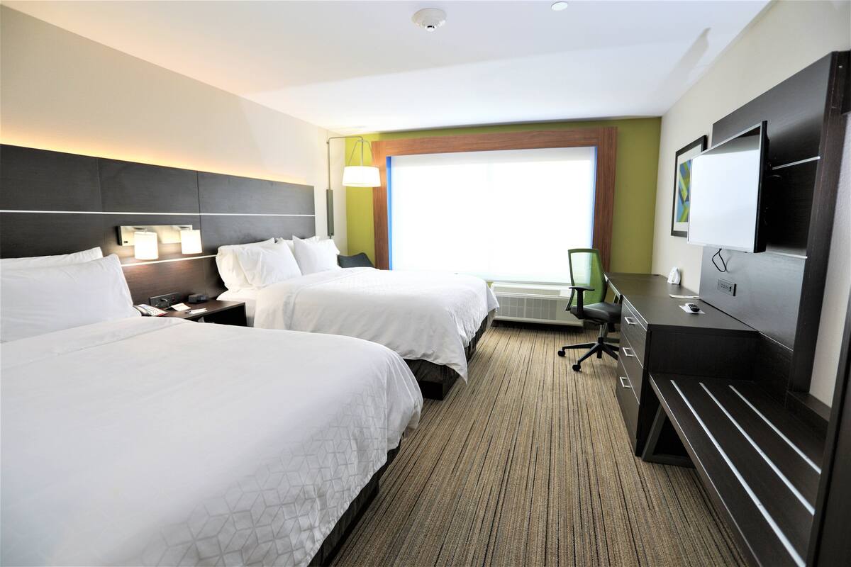 A hotel room with two beds, a desk, a chair, a TV, and a large window.