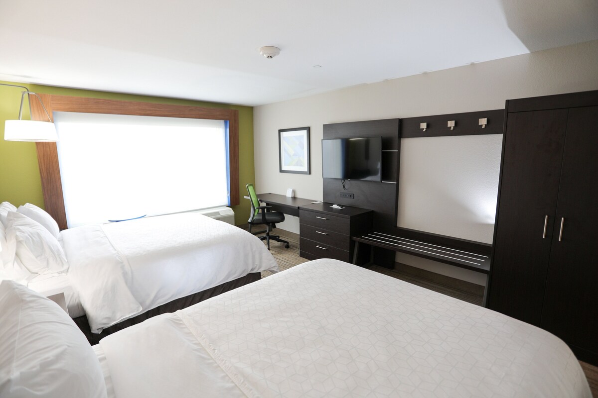 A hotel room with two beds, a desk, a chair, a TV, and a wardrobe.