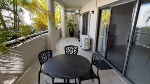 En balkon med et bord, stole og en urtepotte samt en skydedør.