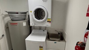 A compact laundry area with a washing machine, dryer, and a sink. - Jubilee Apartment 03 (South West Rocks)