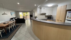 A modern kitchen with a curved countertop, white cabinets, and a microwave. - Jubilee Apartment 03 (South West Rocks)