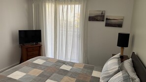 Een slaapkamer met een bed, een televisie op een nachtkastje, een lamp en twee schilderijen aan de muur.