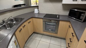 A kitchen with stainless steel appliances, a double sink, and wooden cabinets. - Jubilee Apartment 03 (South West Rocks)