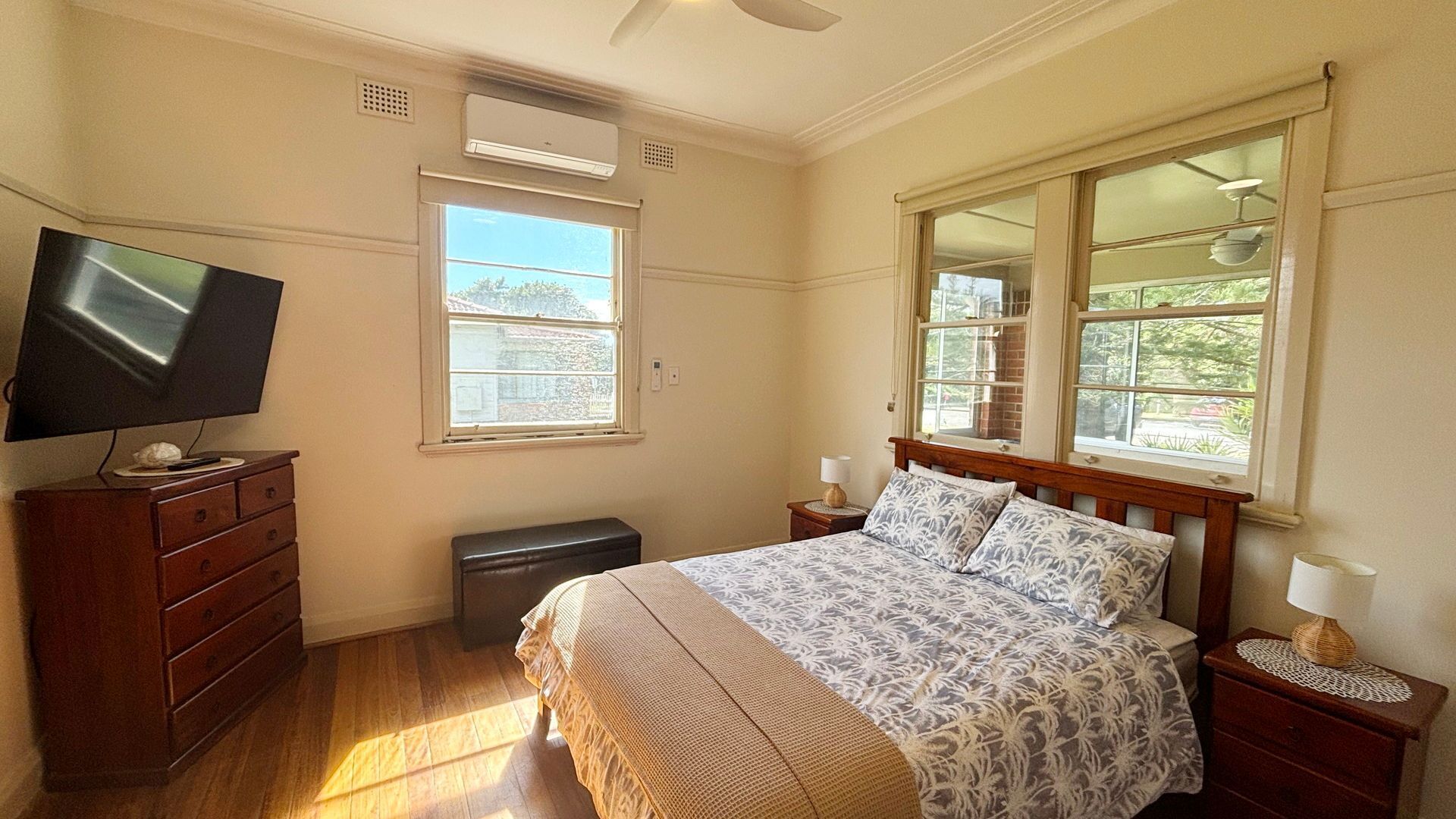 A bedroom with a bed, a television on a dresser, a window, and a ceiling fan.