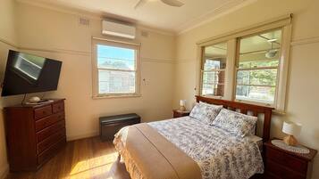 A bedroom with a bed, a television on a dresser, a window, and a ceiling fan.