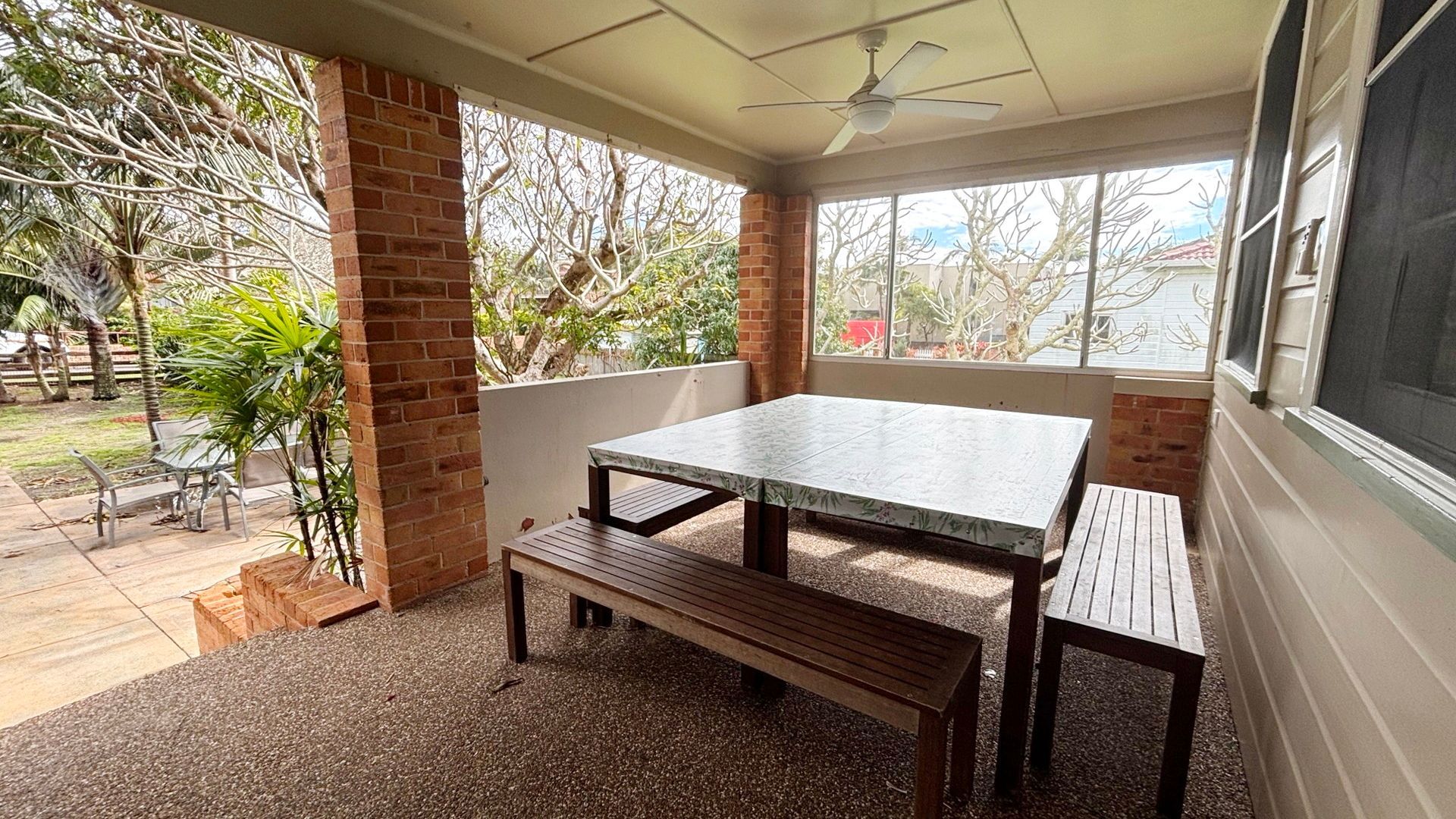 A covered patio area with a table and bench, brick walls, and a view of the outdoors.