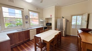 A kitchen with wooden cabinets, a dining table, and a refrigerator. - Yia Yia's Place - walk to the beach (SOUTH WEST ROCKS)