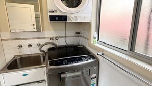 A compact kitchen with a NuClear dishwasher, a black stove, a washing machine, and a window with a view. - Yia Yia's Place - walk to the beach - Bring your own linen (SOUTH WEST ROCKS)