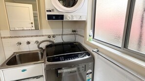 A compact kitchen with a NuClear dishwasher, a black stove, a washing machine, and a window with a view. - Yia Yia's Place - walk to the beach (SOUTH WEST ROCKS)