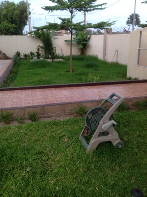 A grassy area with a garden hose and a concrete pathway. - JANJAL Private Mansion (Brufut)