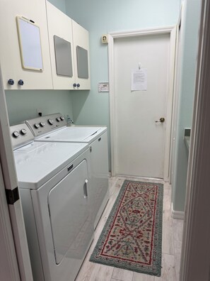 A laundry room with a white washing machine and dryer, a small mirror, and a door with a paper on it.