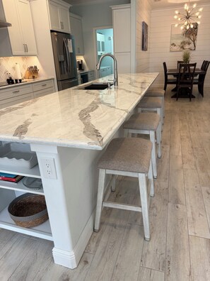 A kitchen with a marble island, white cabinetry, and a dining area with wooden chairs. - Beautiful 3BR Venice Home w/ private pool - OPEN month of January 2027!! (Venice)