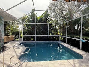 A covered outdoor swimming pool with a metal frame and glass panels, surrounded by lush greenery and a tiled deck. - Beautiful 3BR Venice Home w/ private pool - OPEN month of January 2027!! (Venice)