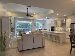 A modern kitchen with a central island, bar stools, and a dining area with a view to the outdoors.