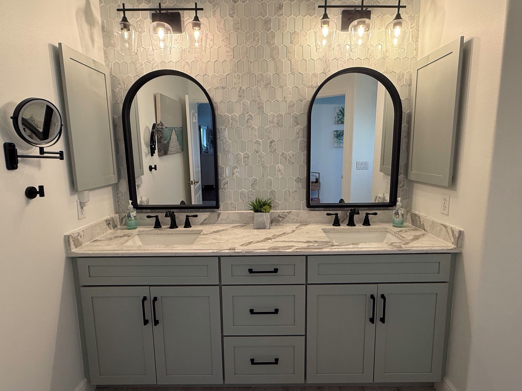 Un baño con tocador doble, dos espejos, encimera de mármol y pared con diseño hexagonal.