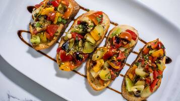 A white plate with four pieces of bruschetta topped with colorful vegetables and a drizzle of sauce.