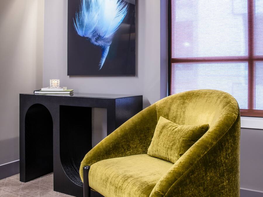 Um quarto com uma poltrona amarela, uma mesa de consola preta com um objeto decorativo e uma obra de arte na parede.