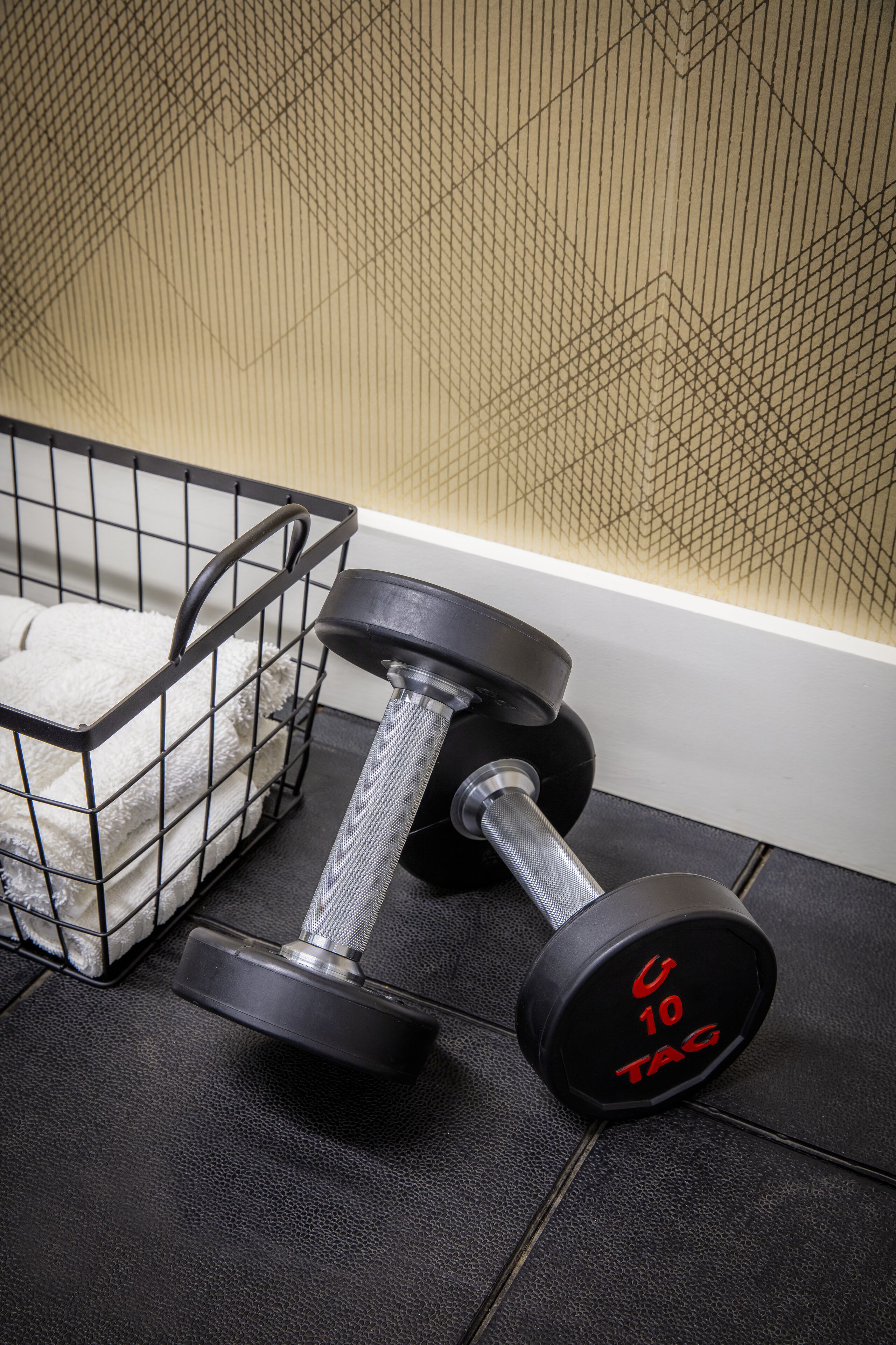 A black metal basket with white towels and a black dumbbell with red text on it.
