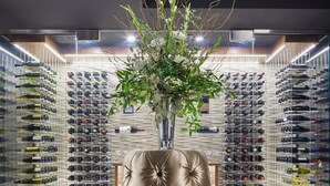 A luxurious leather armchair with a decorative base, positioned in front of a wine cellar with numerous wine bottles and a large vase of greenery. - The Kindler Hotel (Lincoln)