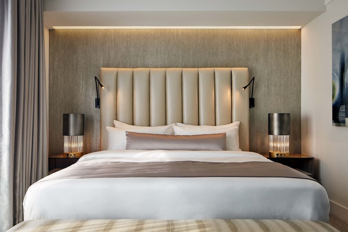 A modern hotel room with a large bed, two bedside tables with lamps, and a textured wall behind the bed.