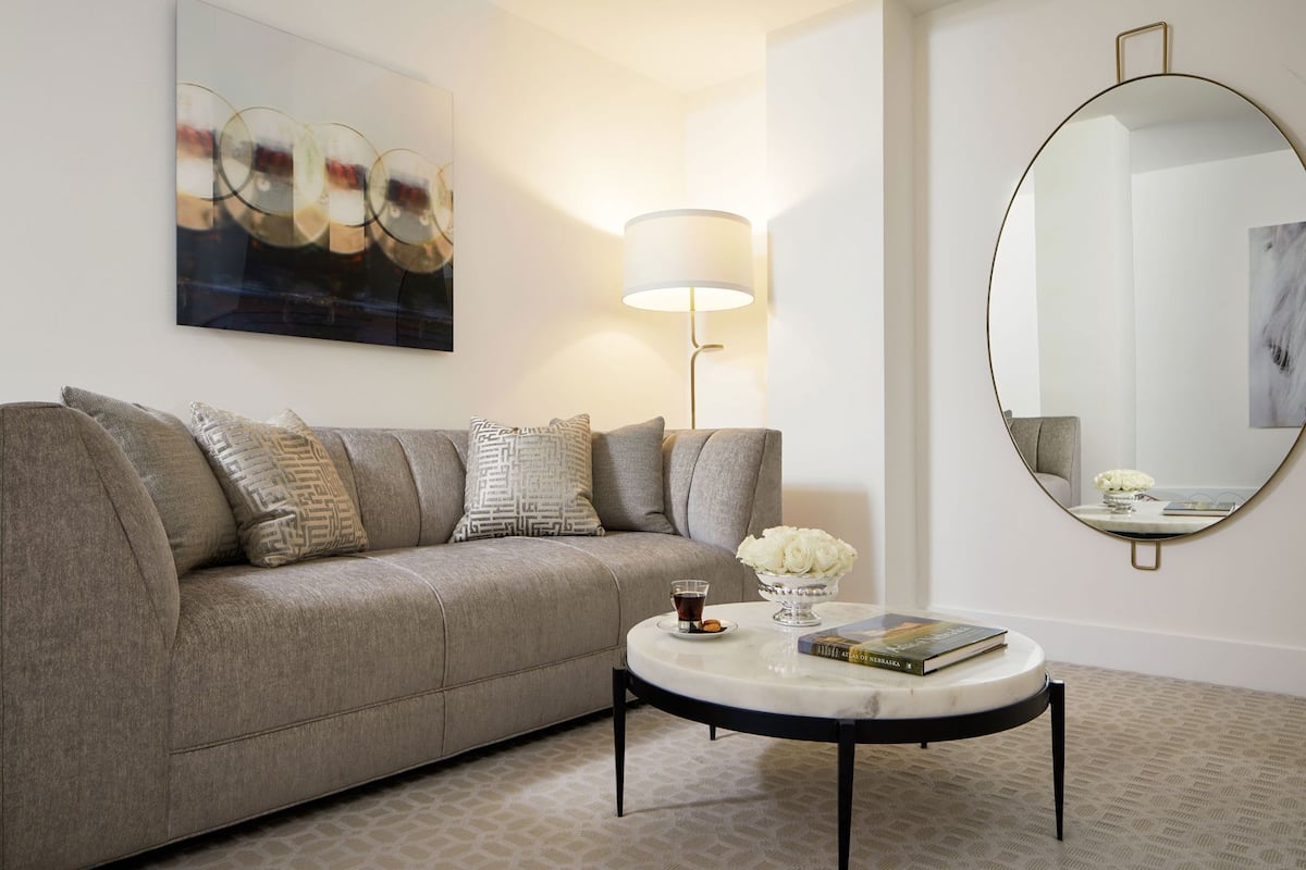 A modern living room with a grey sofa, a round coffee table, a floor lamp, a round mirror, and a painting on the wall.