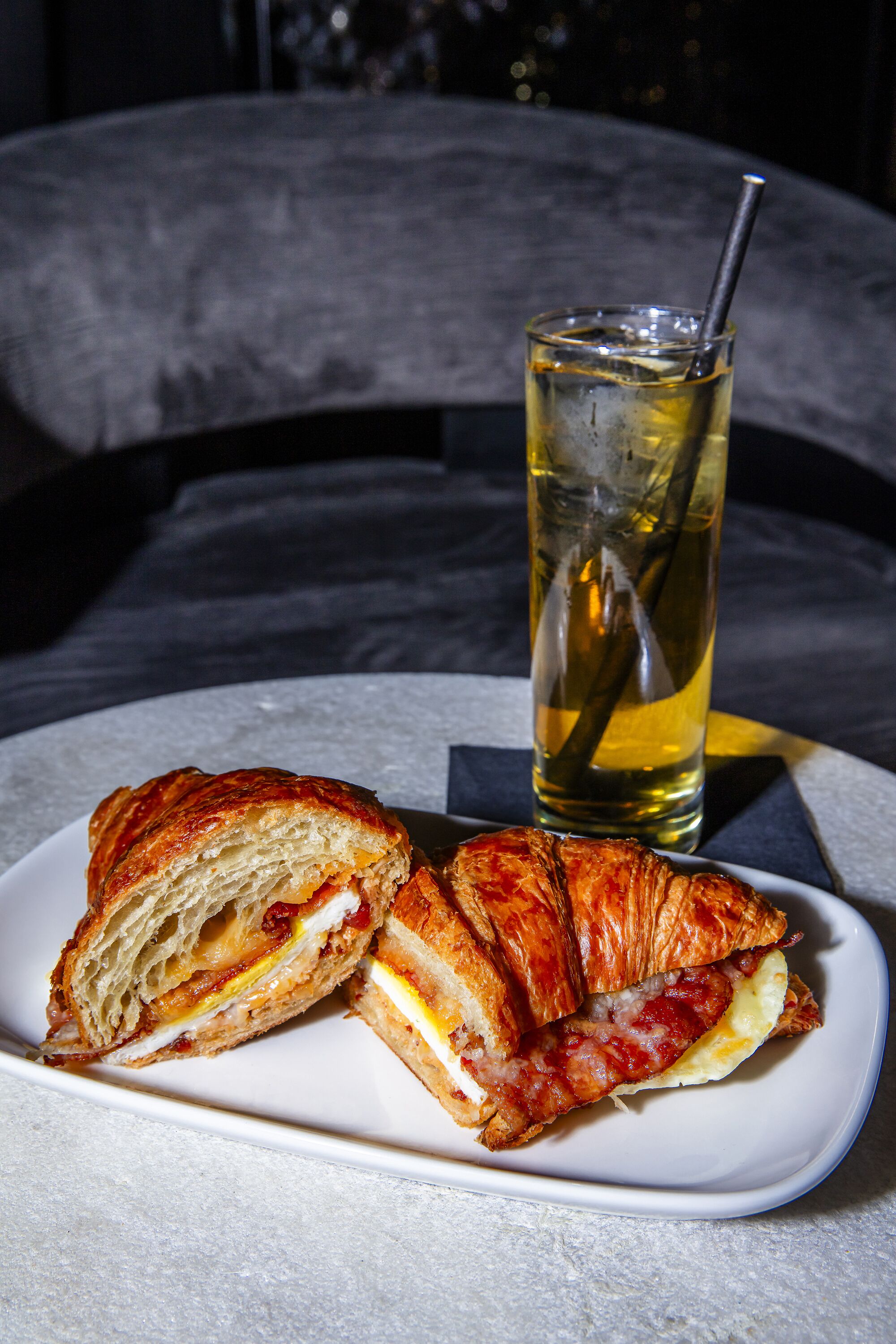 A sandwich on a plate with a drink in the background.