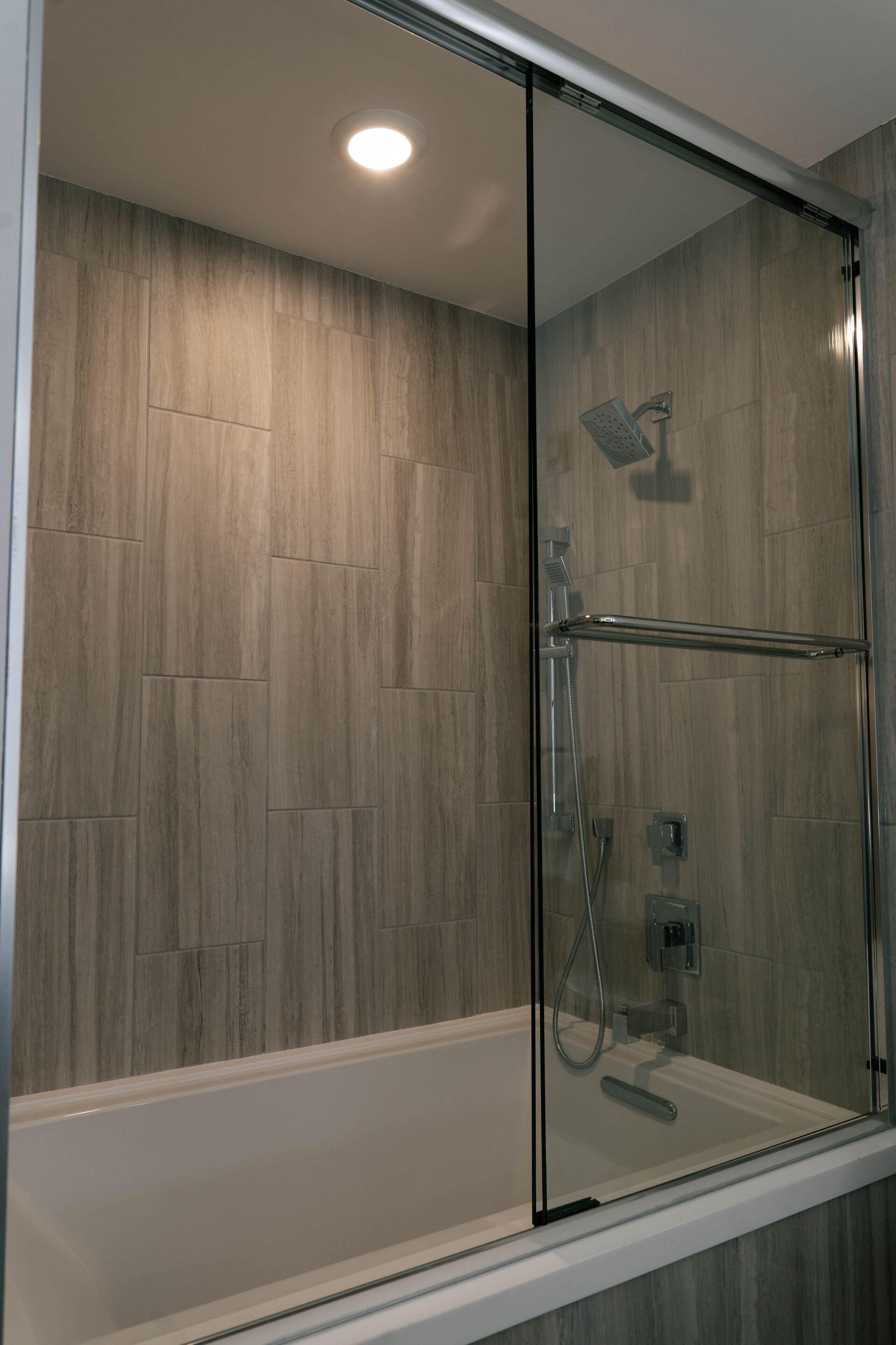 Une douche fermée par des parois en verre, dotée d’un pommeau de douche à main et de commandes à main.