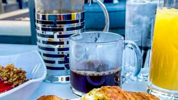 A breakfast setting with a croissant sandwich, a coffee mug, a glass of orange juice, and a pitcher of water.