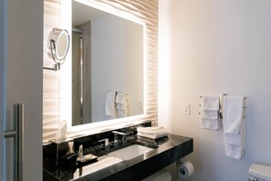 A modern bathroom with a large mirror, black countertop, white towels, and a toilet. - The Kindler Hotel (Lincoln)