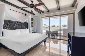 Habitación de hotel con una cama grande, ventilador de techo y balcón con sillas.