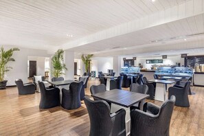 Un restaurante moderno con suelo de madera, sillas tapizadas de color negro y una barra central con vitrina.