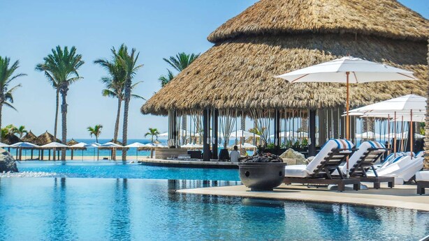 A pool area with thatched-roof structures, lounge chairs, and umbrellas. - Hilton Vacation Club Cabo Azul Los Cabos (San Jose del Cabo)