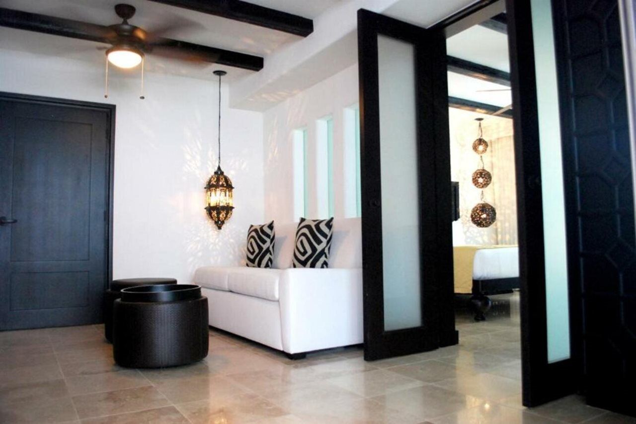 Un salon moderne avec un canapé blanc, des coussins aux motifs noir et blanc, un luminaire suspendu et une porte sombre.