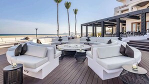 A rooftop lounge with white sofas and round tables, overlooking a beach with palm trees and a clear sky. - Hilton Vacation Club Cabo Azul Los Cabos (San Jose del Cabo)