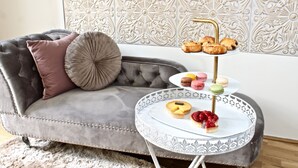 A grey tufted sofa with a decorative pillow, a round side table with a white and gold patterned tray holding pastries and macarons, and a wall with intricate floral tile design. - NEW DESIGN & STYLE Apartment Old Town XXL (Prague)