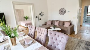 A modern living room with a sectional sofa, a dining area with a table set for two, and a large wall clock. - NEW DESIGN & STYLE Apartment Old Town XXL (Prague)