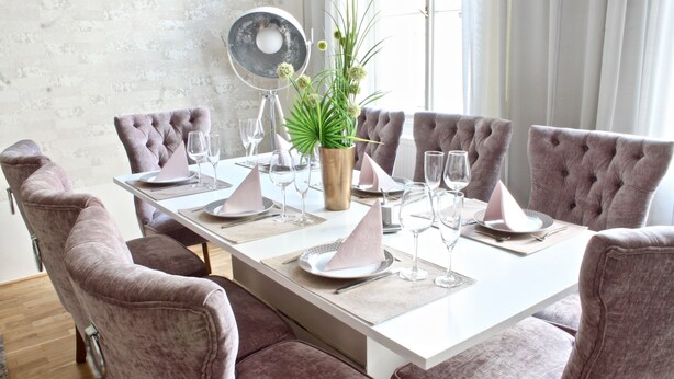 A dining table set with pink upholstered chairs, a vase with green plants, and wine glasses. - NEW DESIGN & STYLE Apartment Old Town XXL (Prague)