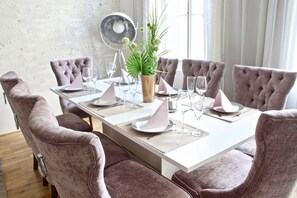 A dining table set with pink upholstered chairs, a vase with green plants, and wine glasses.