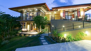 Una moderna casa a due piani con un patio spazioso, ampie finestre e un giardino curato.