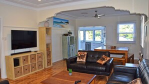 Una sala de estar con televisor, un sofá de cuero negro, una mesa de centro y una cocina visible a través de una puerta abierta.