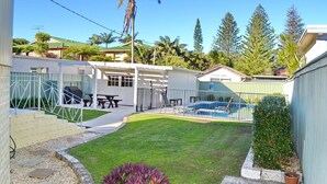 Un patio trasero con piscina, un porche cubierto y un pequeño césped.