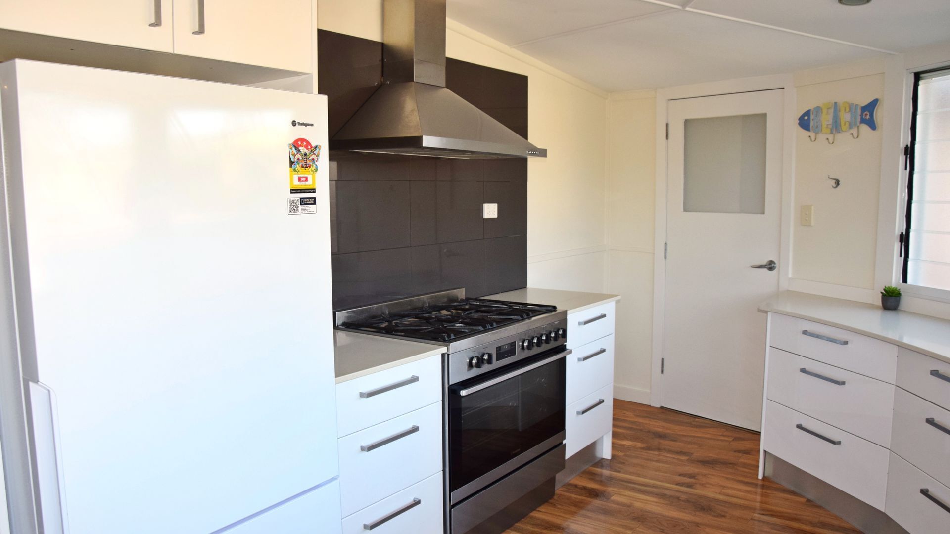 Una cocina moderna con armarios blancos, una campana extractora de acero inoxidable, una estufa a gas y un horno.