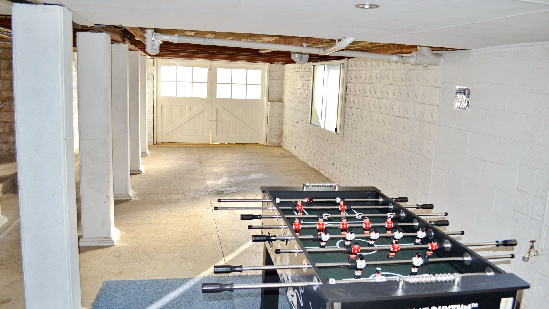Una habitación con dos mesas de fútbol de mesa, un ventanal y una puerta que da a un espacio exterior.