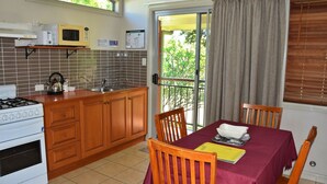 A kitchen with wooden cabinets, a gas stove, a microwave, and a sink. There is a dining table with chairs and a window with curtains. - Coast & Country Cabin 2 (RAINBOW REACH)