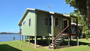 A green house with a balcony and a staircase, situated near a body of water. - Coast & Country Cabin 2 (RAINBOW REACH)